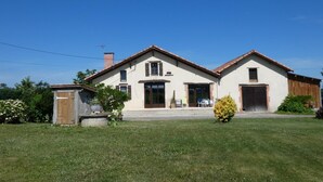 Ein zweistöckiges Haus mit Veranda, Garage und einem kleinen Gartenhaus.