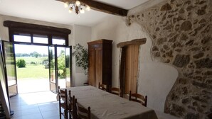 Ein Esszimmer mit einem großen Tisch, sechs Holzsesseln, einer Kristallleuchter, Steinwänden und Blick auf eine grüne Landschaft durch eine Glastür.