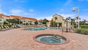 A pool area with lounge chairs, a hot tub, and a building with a red-tiled roof.