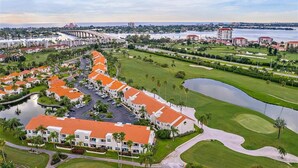 A golf course with a water hazard, a bridge, and a row of buildings with red roofs.