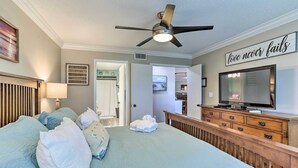 A bedroom with a bed, a ceiling fan, a TV, and a motivational quote on the wall.