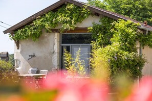 Un bâtiment rustique, doté d’un toit en pente, de murs couverts de lierre et d’un petit porche avec deux chaises.