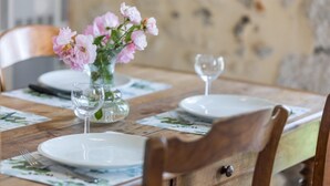 Une table à manger dressée avec des assiettes, un vase de fleurs et des verres à vin.