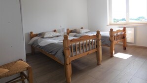 Une chambre avec un lit en bois, une petite chaise en bois, un luminaire suspendu et une grande fenêtre.