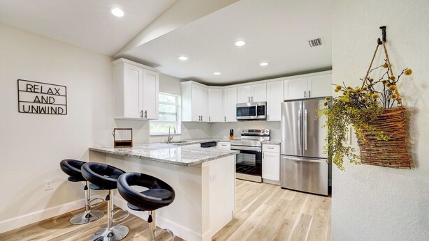 A modern kitchen with white cabinets, stainless steel appliances, and a central island with bar stools. - 1 Mi to Links! Resort Home Near Raceway in Sebring (Sebring)