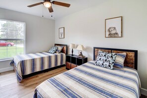 Una camera da letto con due letti, un ventilatore a soffitto, una finestra che si affaccia su un'auto rossa e un comodino con lampade.