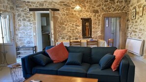 Una sala de estar acogedora con una pared de piedra, un sofá azul con cojines rojos, una mesa de centro de madera y una lámpara colgante.