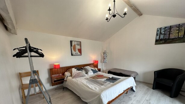 Une chambre à coucher comprenant un lit, des tables de chevet, une chaise, un porte-manteau mural et un tableau accroché au mur.
