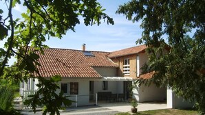 Une maison à deux étages avec un toit en tuiles, un patio couvert avec des sièges et un petit jardin.