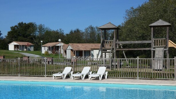 Ein Schwimmbecken mit Liegestühlen und einer Holzspielanlage.