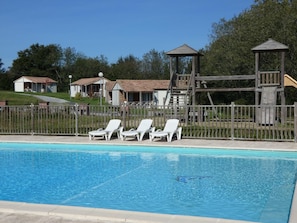 En pool med solstolar, en lekställning i trä och hus i bakgrunden.