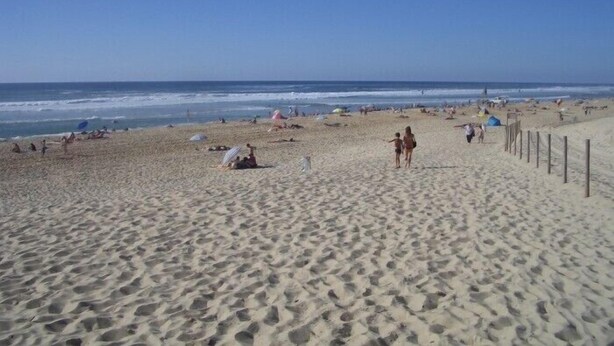 Een breed zandstrand met mensen en parasols, een heldere lucht en de oceaan op de achtergrond.