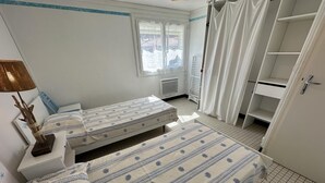 Een kamer met twee bedden, een raam, een radiator en een witte inbouwkast.