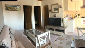 Una sala de estar con un sofá, una mesa de centro y un televisor. Hay una cocina con estufa, microondas y alacenas.