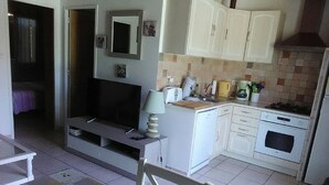Un espacio habitable compacto con kitchenette, comedor y un televisor pequeño.