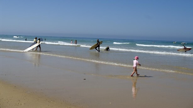 Escena de playa con gente caminando y haciendo surf.