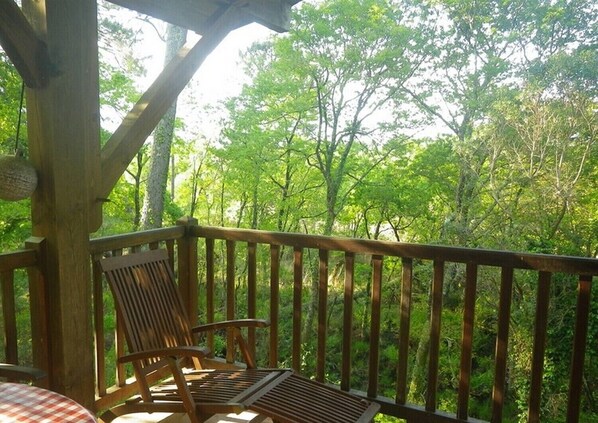 A wooden deck with a wooden chair and a table, surrounded by lush green trees.