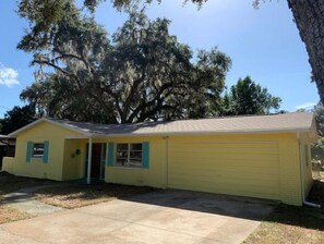 A yellow single-story house with a garage, surrounded by trees and a clear sky. - Gospel Island Getaway (Inverness)