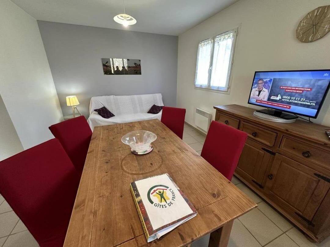 A dining area with a wooden table, red chairs, a white sofa, a television, and a cabinet.