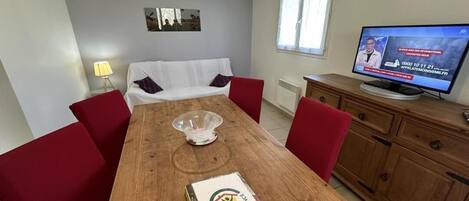 A dining area with a wooden table, red chairs, a white sofa, a television, and a cabinet.