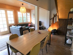 Ein Essbereich mit Holztisch und Stühlen, einer Couch und einem Fernseher im Hintergrund.