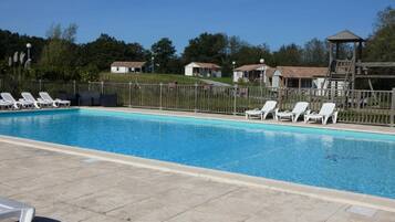 Una piscina con sillones blancos y una terraza de madera.