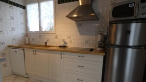 A kitchen with white cabinets, a stainless steel refrigerator, a microwave, and a window with blinds.