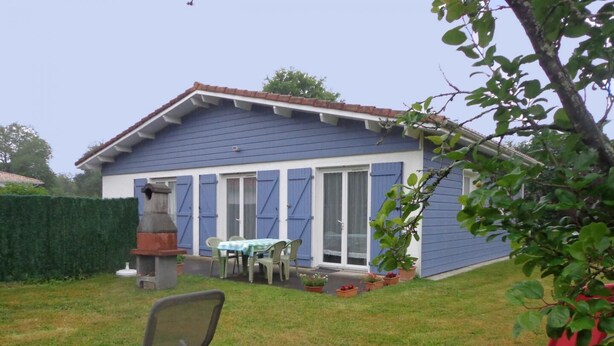 A house with a blue exterior, a patio with a table and chairs, and a barbecue grill.