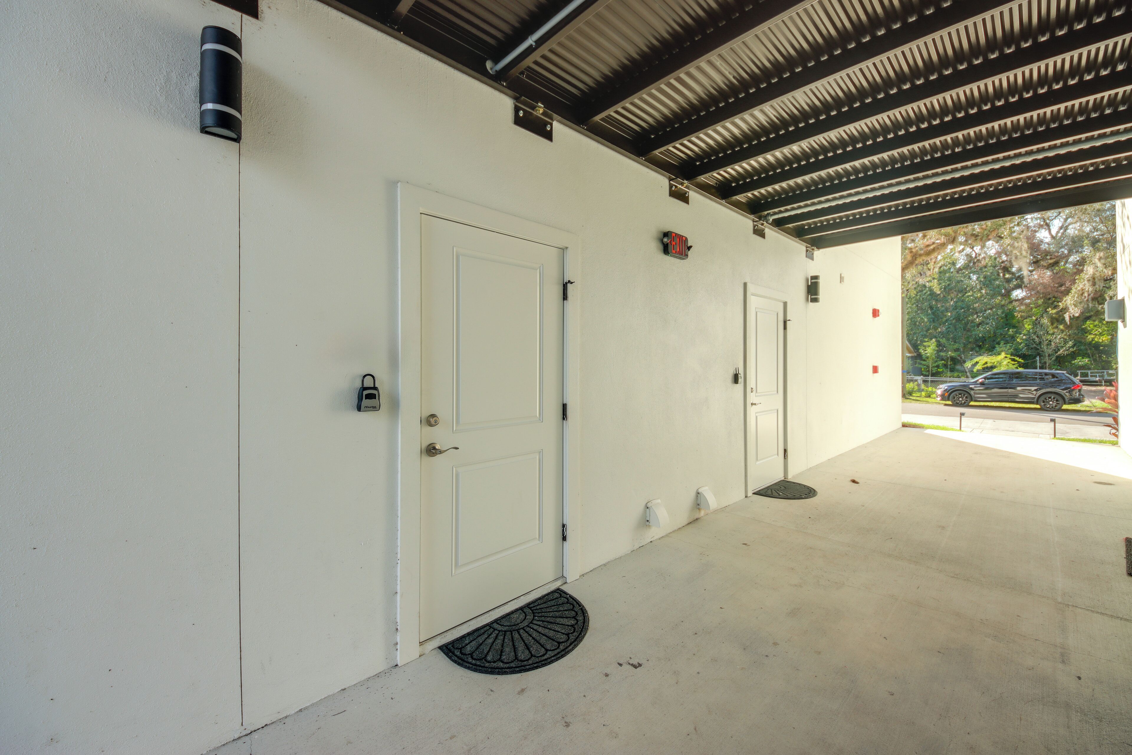 A covered parking area with two white doors, a metal roof, and a visible street with cars.