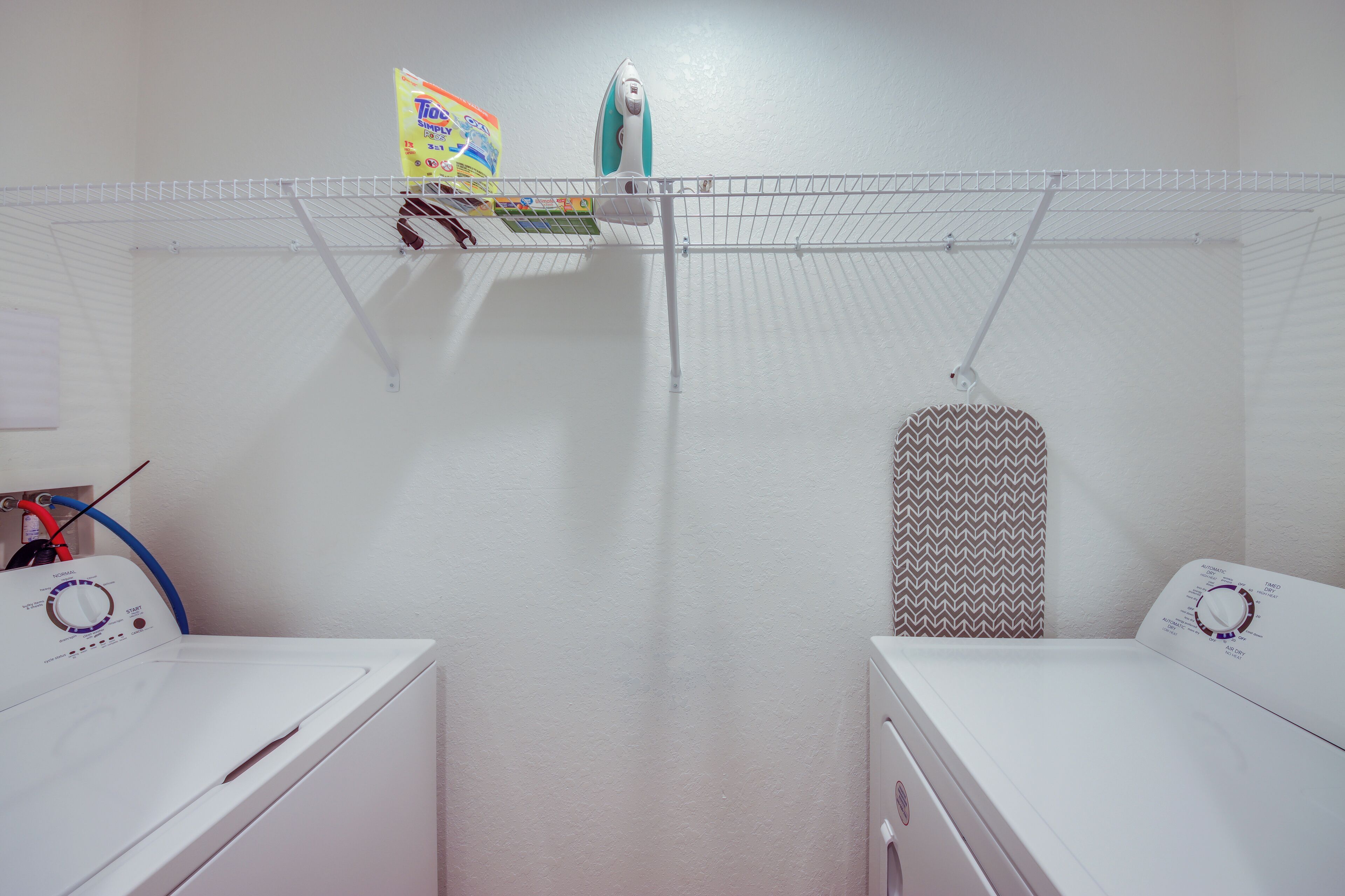 A laundry area with two white washing machines, a drying rack, and a hanging iron.