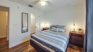 Un dormitorio con una cama, una mesita de noche, un espejo, un ventilador de techo y una puerta.