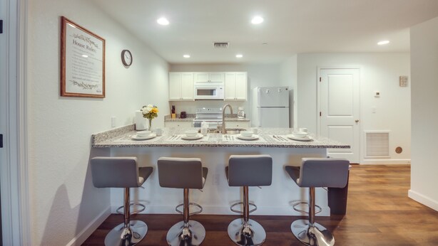 Una cocina moderna con armarios blancos, encimera de granito y cuatro taburetes de bar.