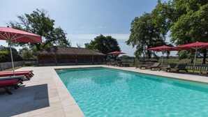 A swimming pool with lounge chairs and umbrellas, surrounded by trees and a wooden building. - Vieux Chêne - Vert - Gîte (VERT)