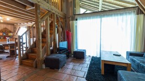 A spacious living area with a wooden staircase, a television, and a sofa. - Vieux Chêne - Vert - Gîte (VERT)