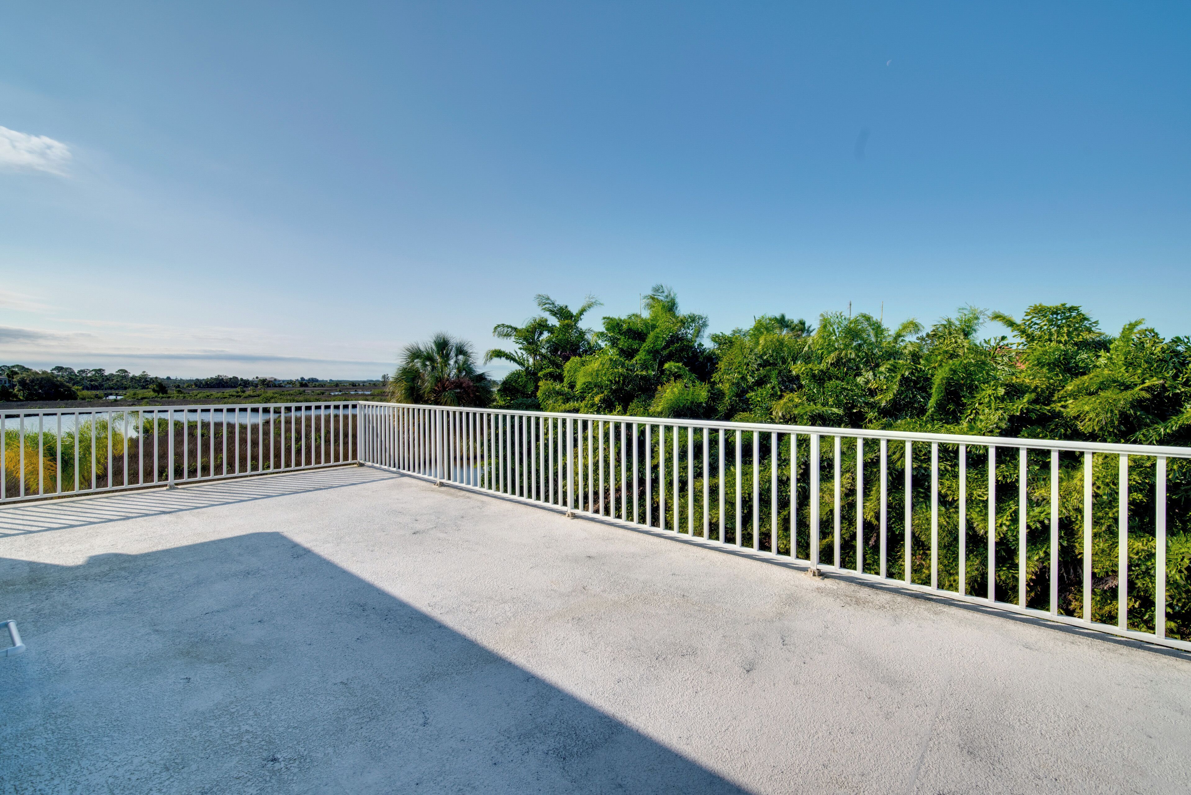 A concrete balcony with a white metal railing overlooking a lush green landscape.