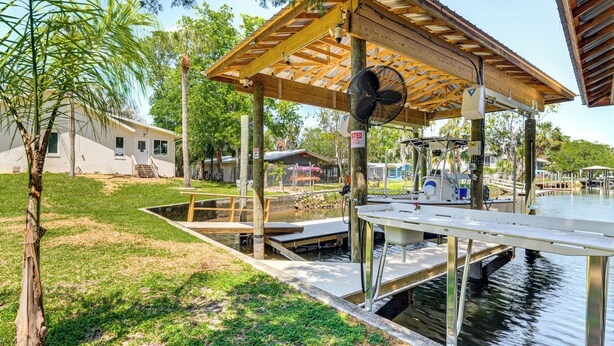 A covered dock area with a fan, a boat, and a small building in the background. - Canal-front Retreat in Crystal River! (Crystal River)