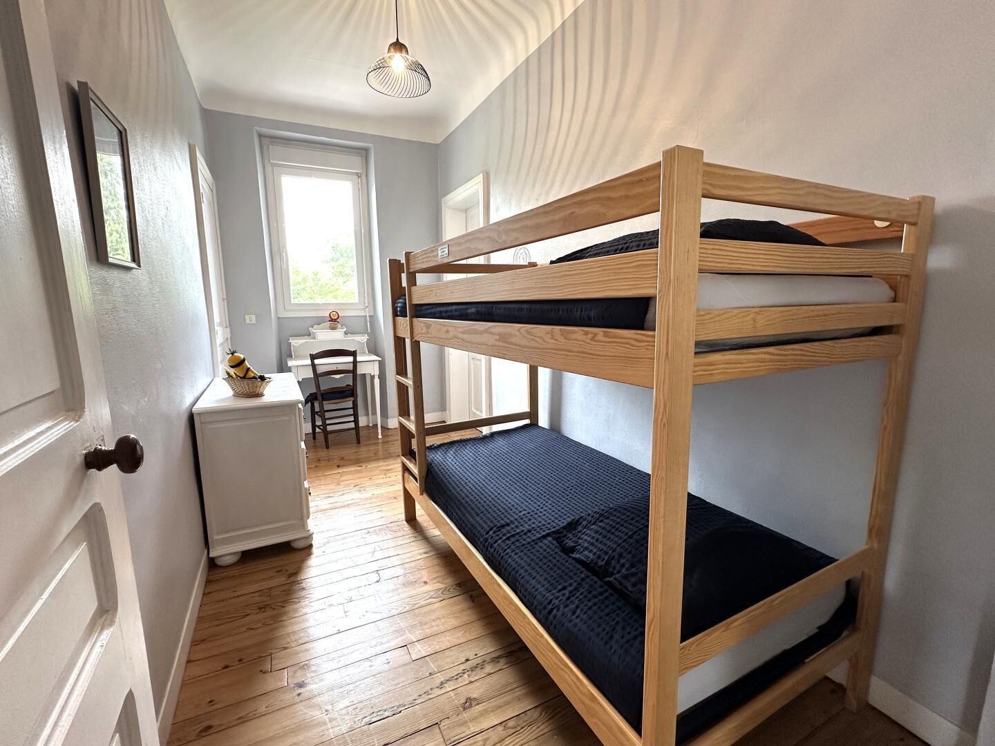 A bunk bed with a desk and chair, a window, and a door.