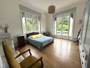 Un dormitorio con cama, una silla, cómoda y ventanas amplias.