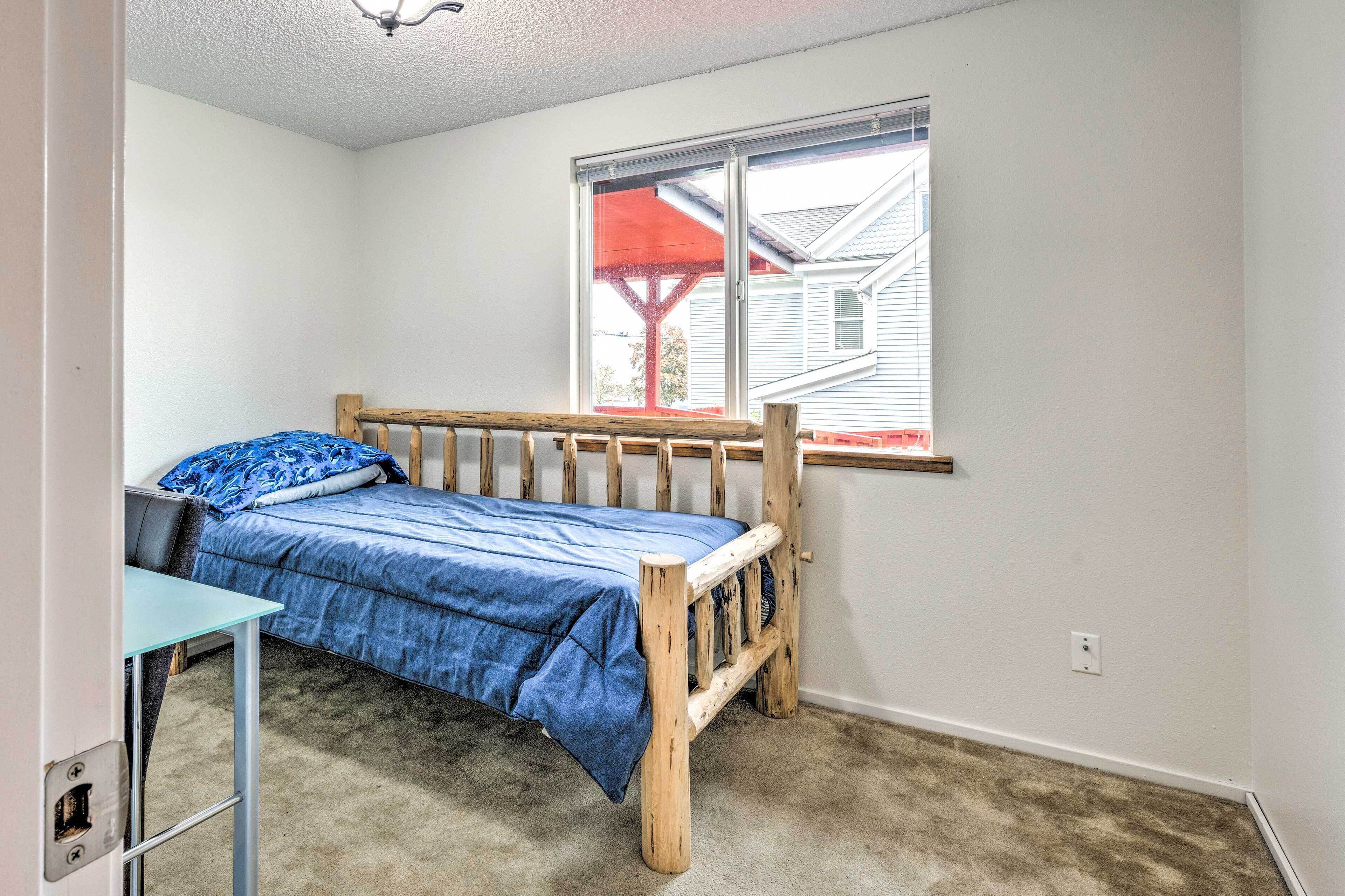 A small, single-bed room with a wooden headboard, a window with a view of a house, and a small table.