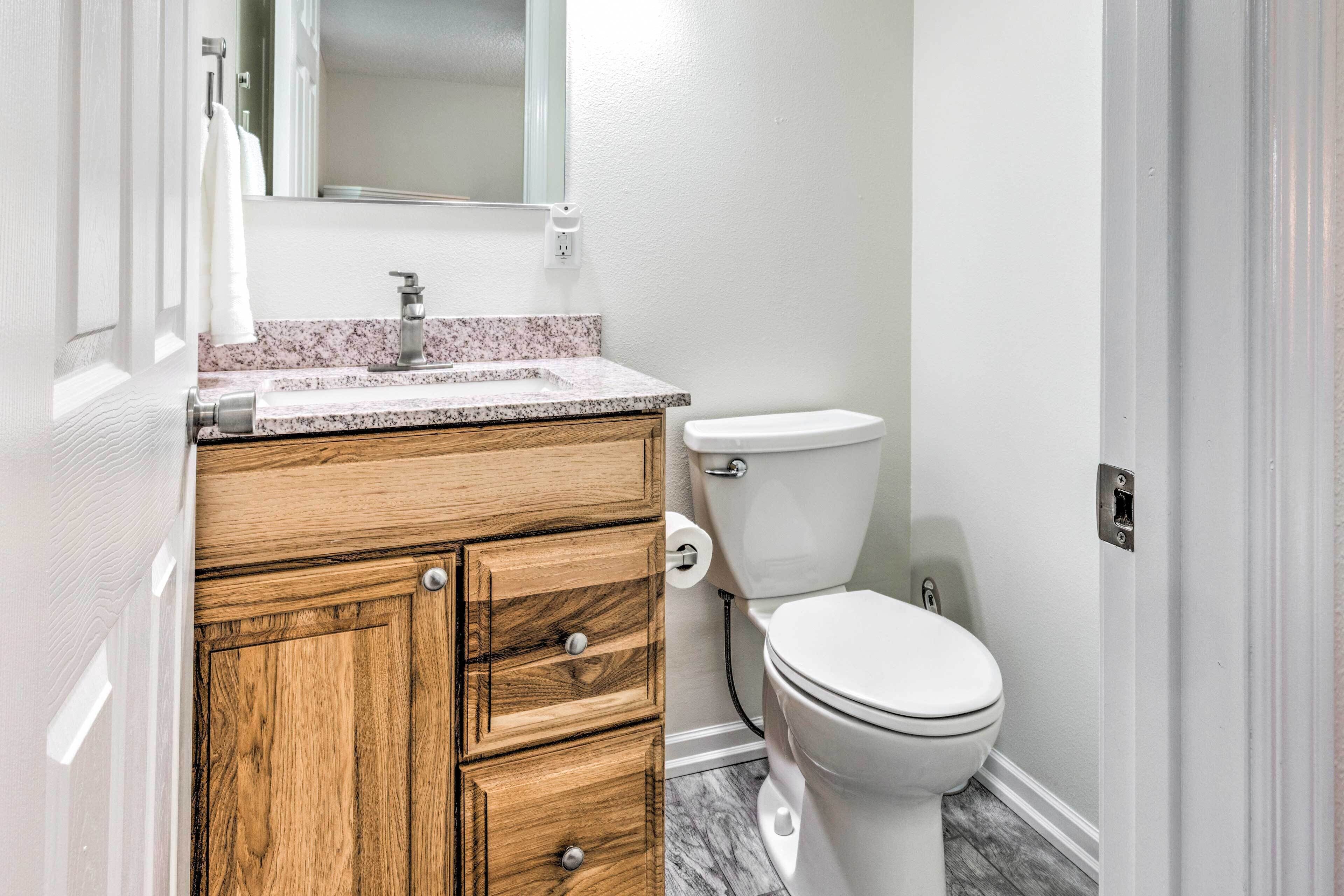 A bathroom with a wooden vanity, a white toilet, and a marble countertop.