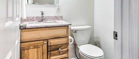 A bathroom with a wooden vanity, a white toilet, and a marble countertop.