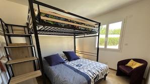 Habitación con literas, una colcha estampada, una silla y ventana con vistas a la vegetación.