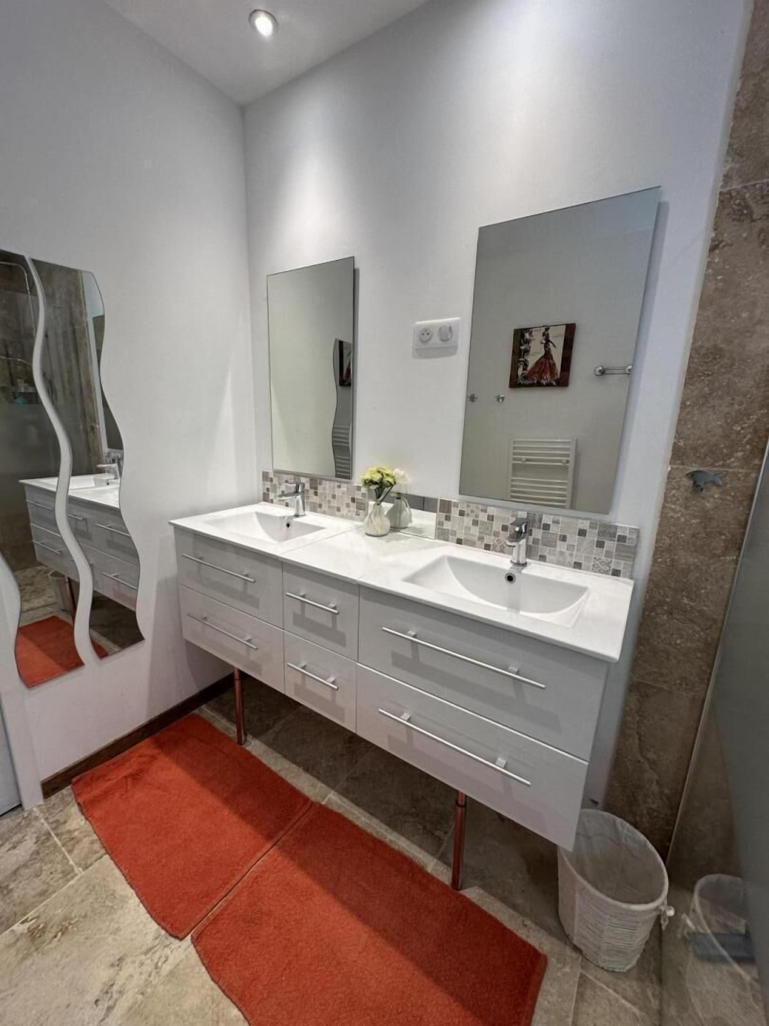A modern bathroom with two sinks, a large mirror, and a red rug.