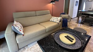 Un salón con un sofá color beige, una mesa de centro con un control remoto, y una pared decorada con tres cuadros.