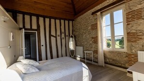 Ein Schlafzimmer mit Bett, Spiegel, einem kleinen Tisch und einem Fenster mit Blick auf Grünflächen.