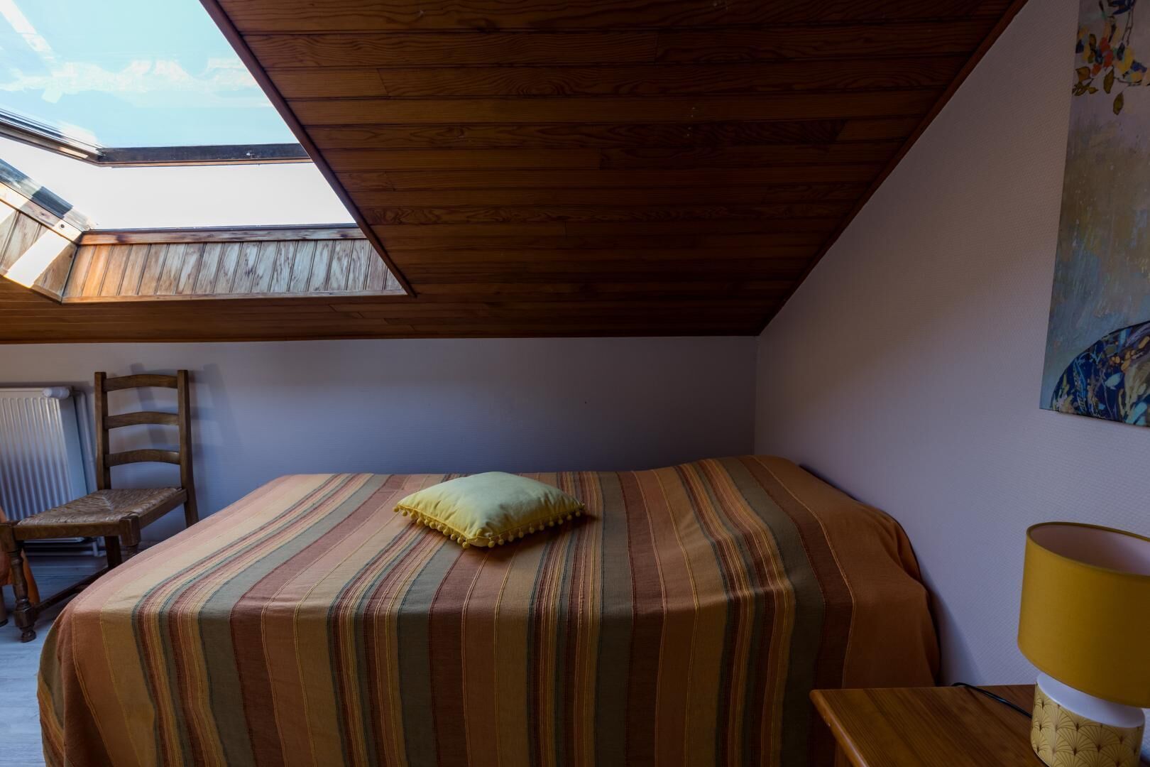 A bedroom with a bed, a chair, a lamp, and a painting on the wall.