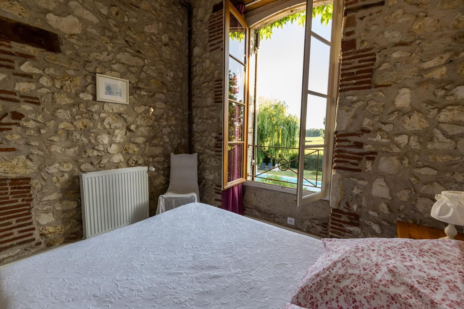 Habitación con paredes de piedra, una cama, un radiador y una ventana con vistas a zonas verdes.
