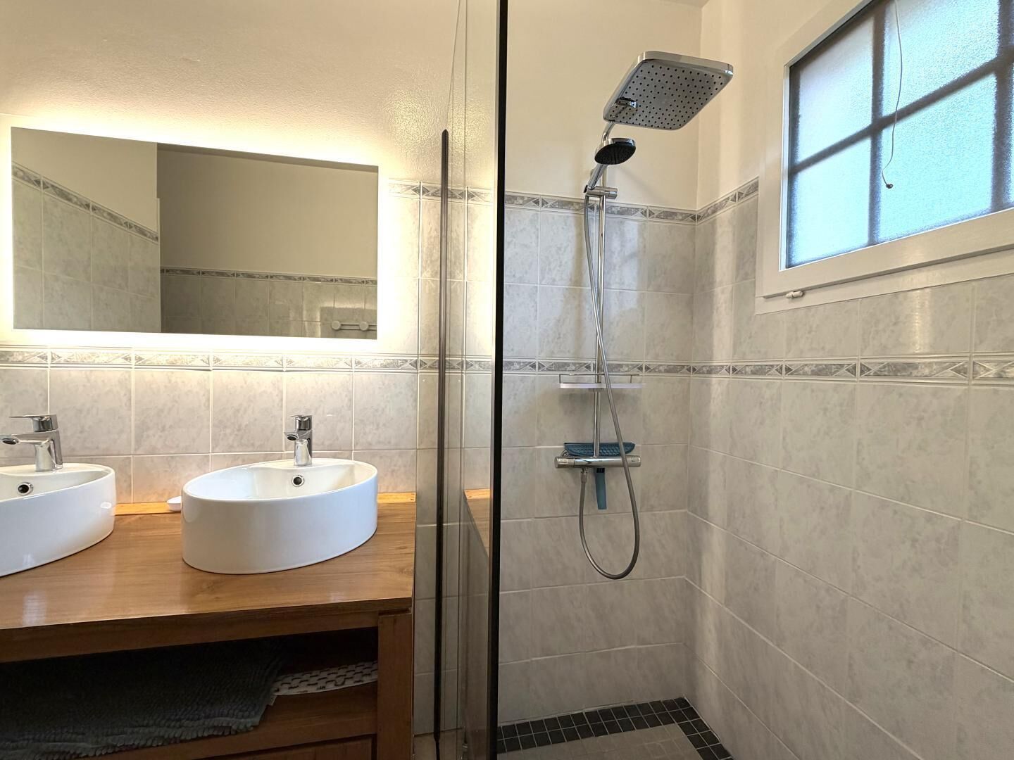 A bathroom with two sinks, a shower, a mirror, and a window.
