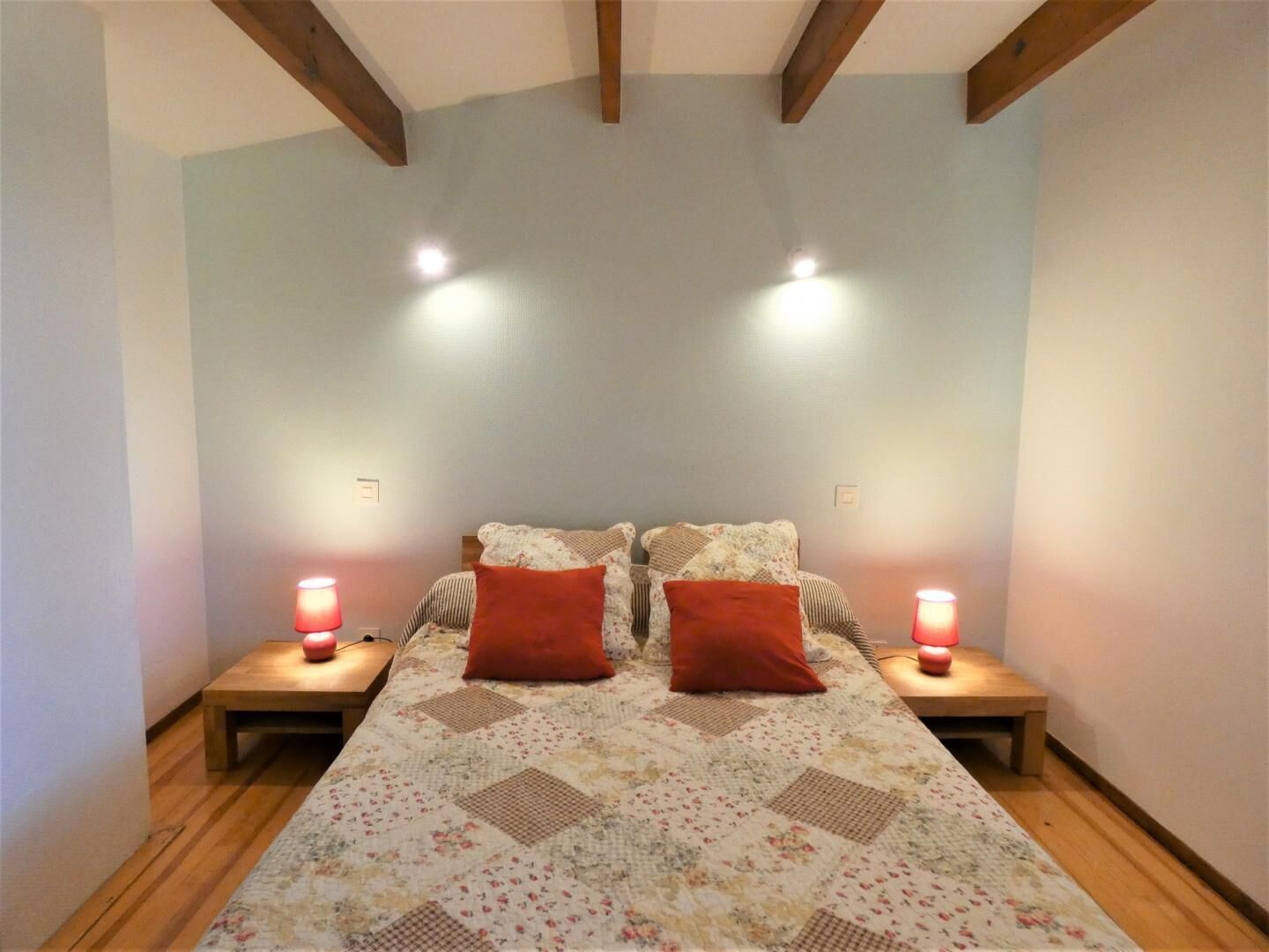 A bedroom with a bed, two nightstands, two bedside lamps, and wooden beams on the ceiling.