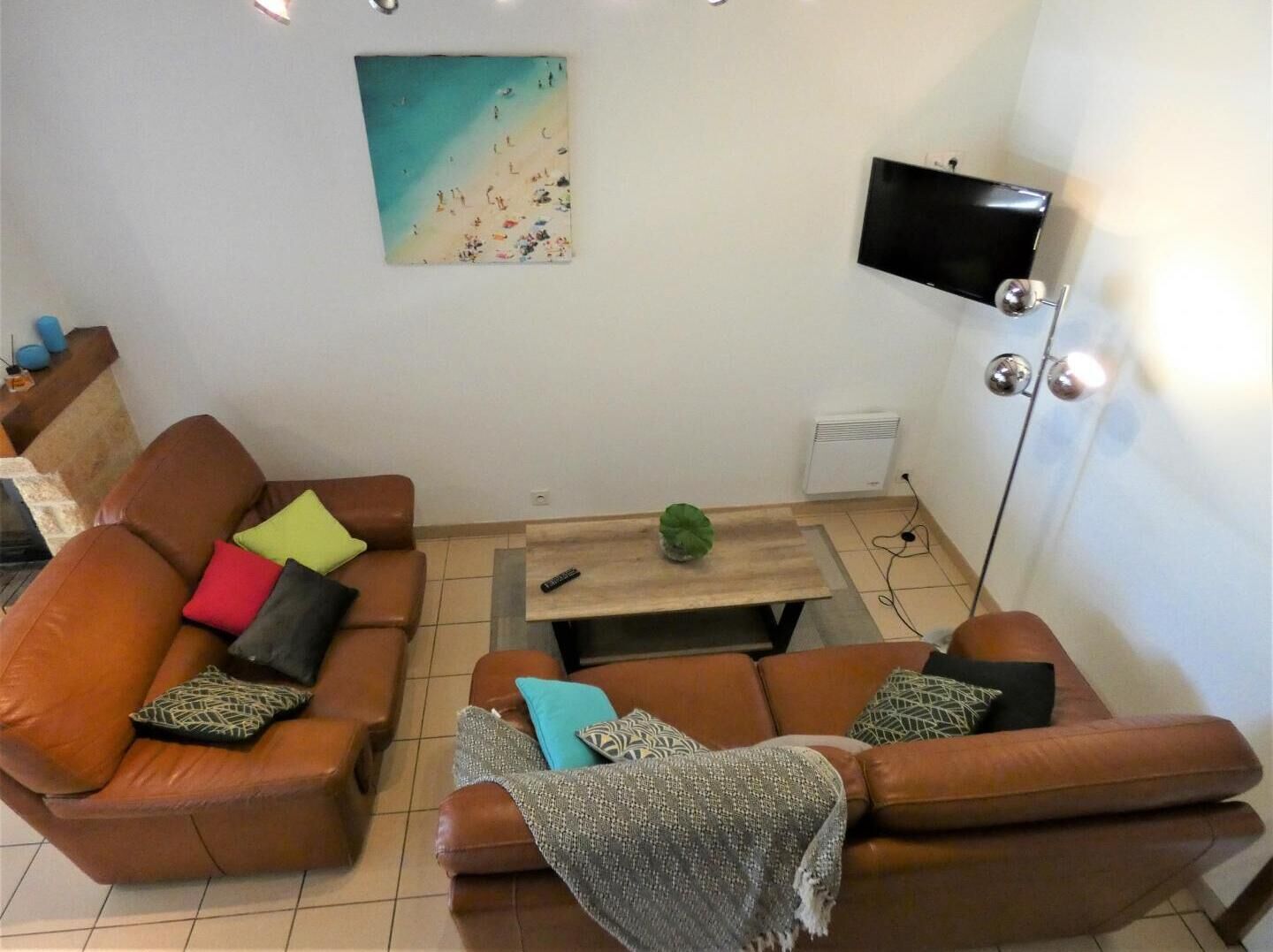 A living room with two brown leather sofas, a wooden coffee table, a TV on a stand, and a painting on the wall.